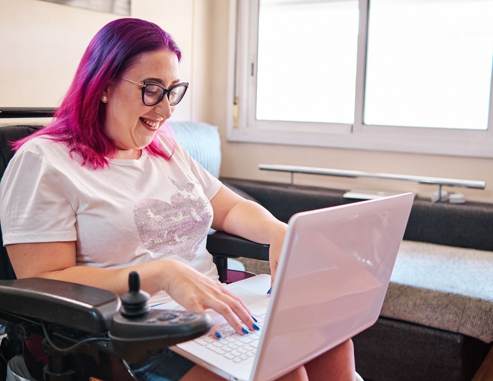 Woman entrepreneur in wheelchair smiling and interacting with business network on laptop